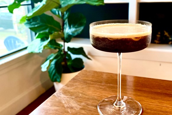 a coffee cocktail in a coupe glass on a wooden table with a fiddle leaf fig in the background